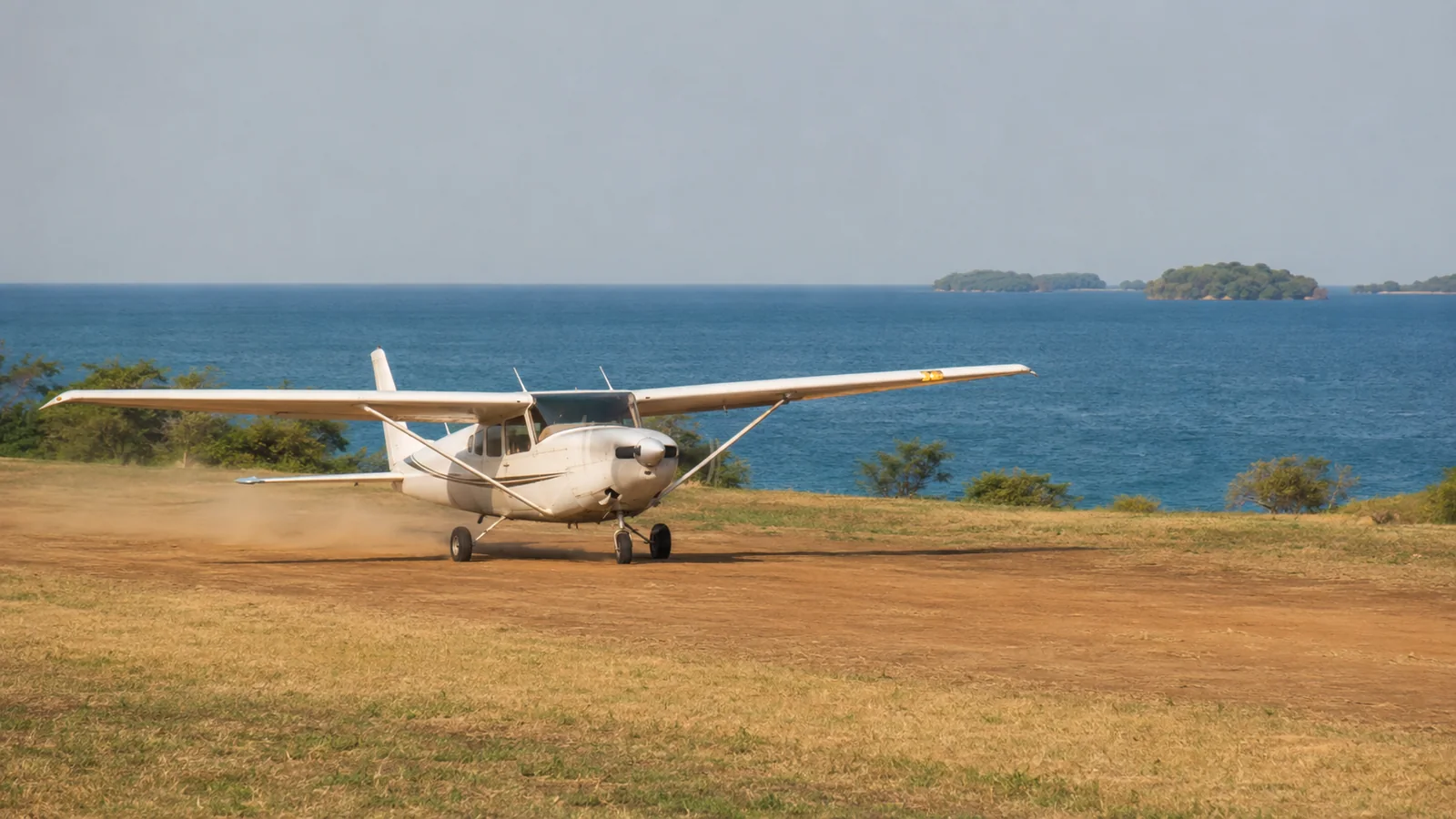 Light aircraft landing on a grass airstrip near Lake Malawi with the blue lake stretching to the horizon behind, scenic Malawi transfer travel photography