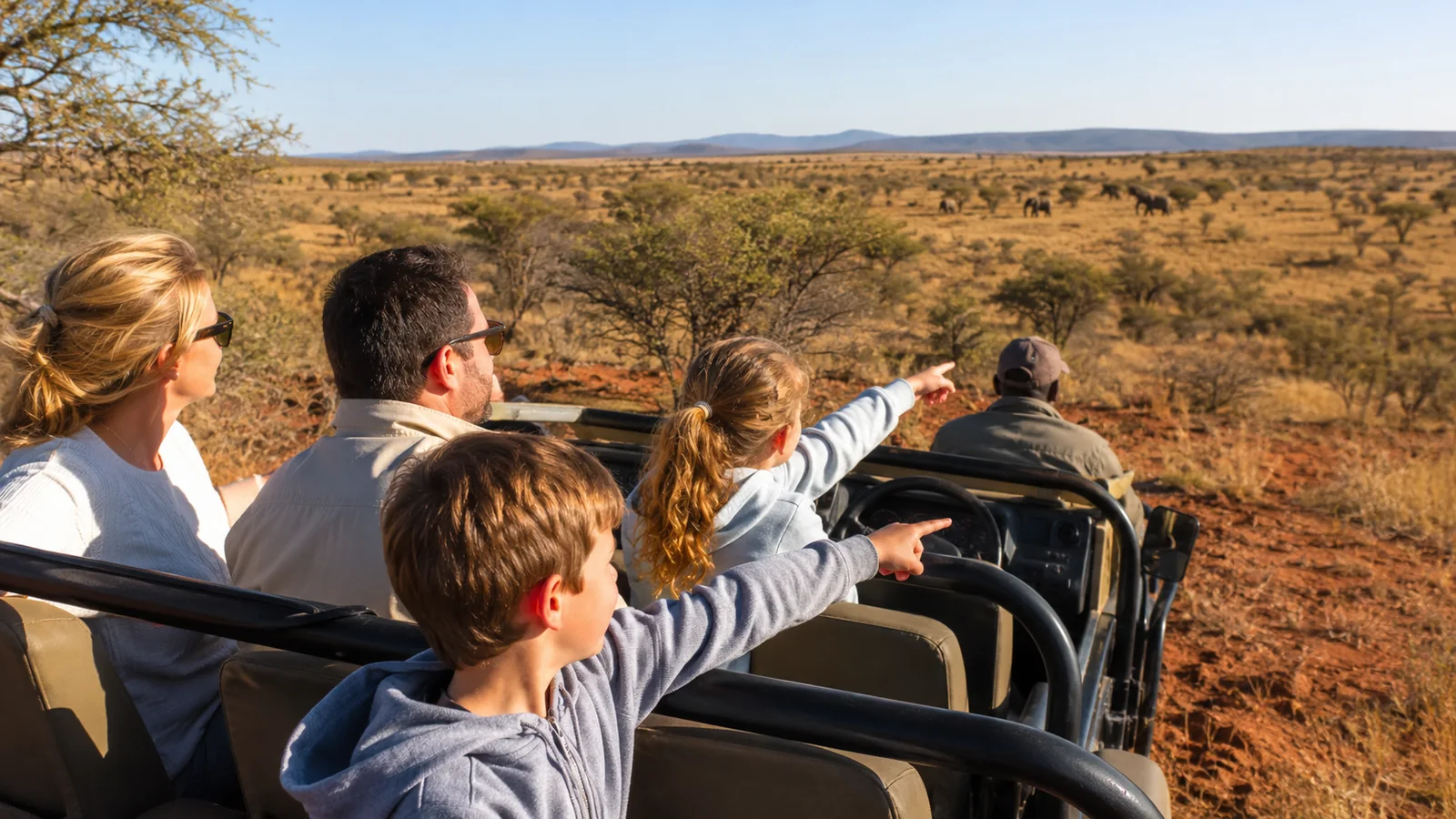 Family on an open safari vehicle in Madikwe Game Reserve with children pointing excitedly at wildlife in a malaria-free South African bushveld, family safari travel photography