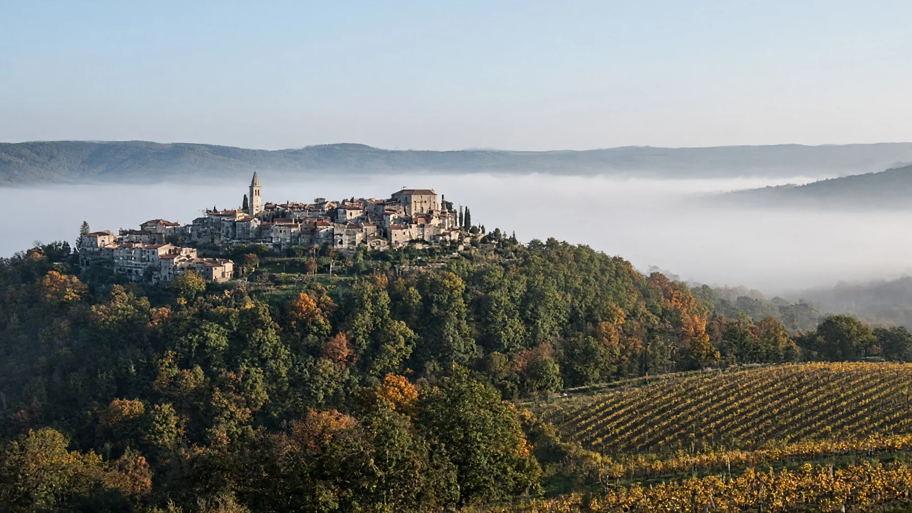 Hilltop stone town above oak woodland and vineyards in autumn colour with morning mist in the valley below, editorial travel photography