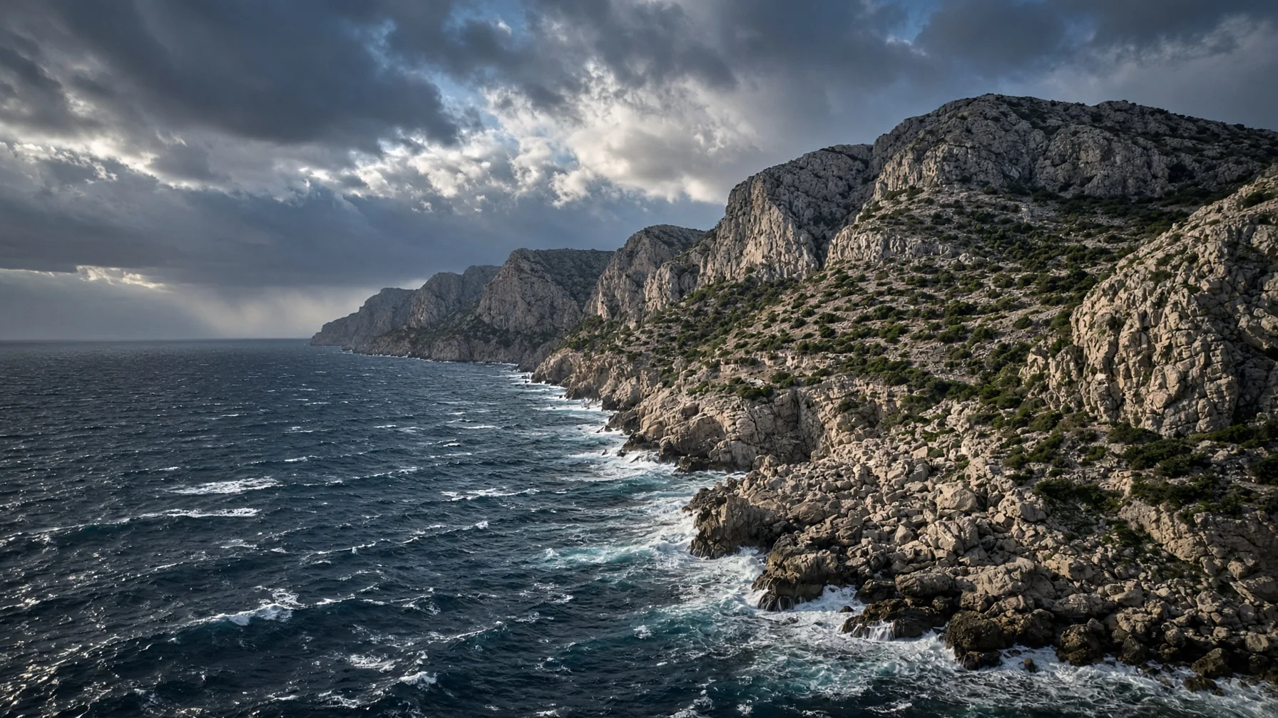 Wind driven whitecaps against a rocky coastline with bare limestone slopes and dramatic winter light over the sea, editorial travel photography