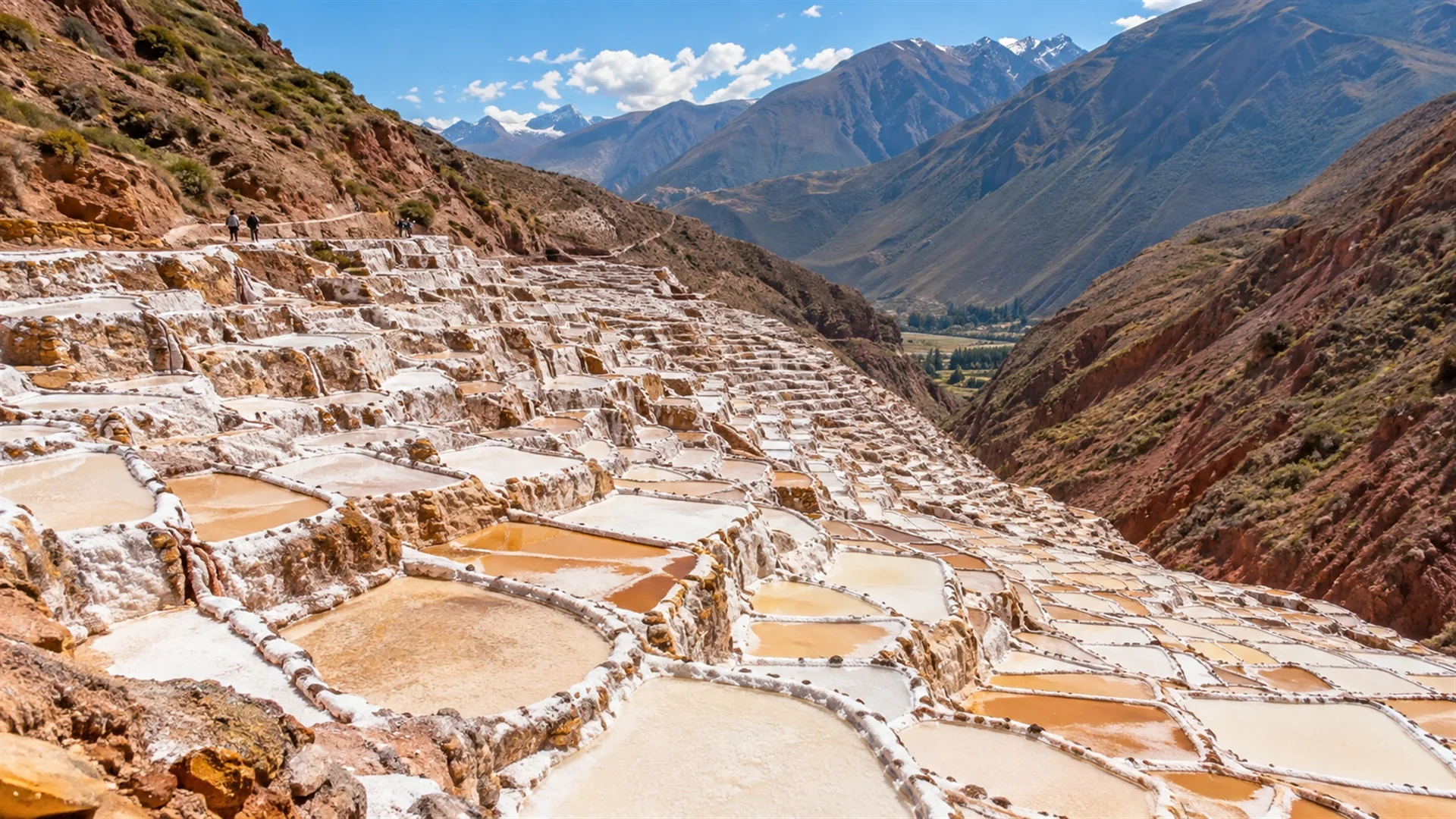Maras salt pans cascading down an Andean hillside in hundreds of white and ochre pools, bright midday sun, aerial style editorial travel photography