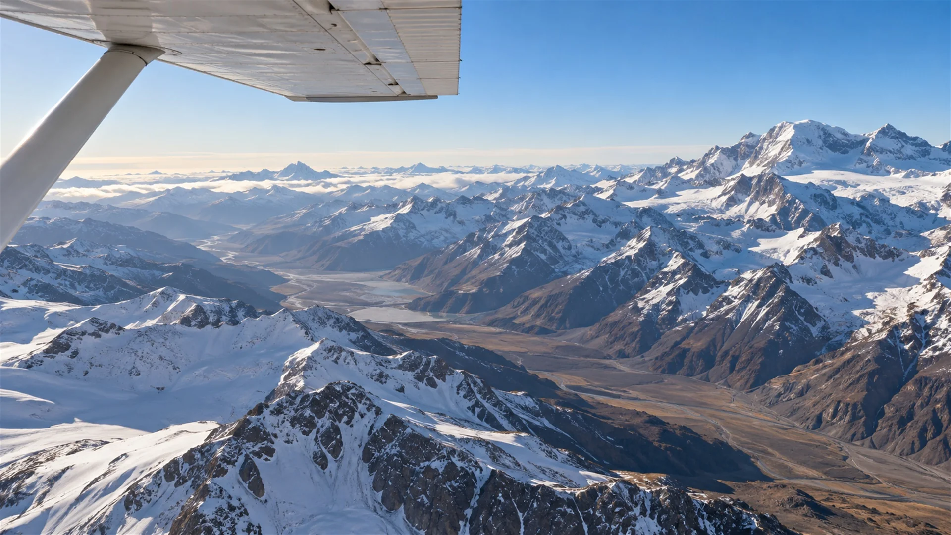 Latin America luxury travel: small aircraft wing above snow-capped Andes peaks and high valleys in clear morning light, aerial luxury travel photography