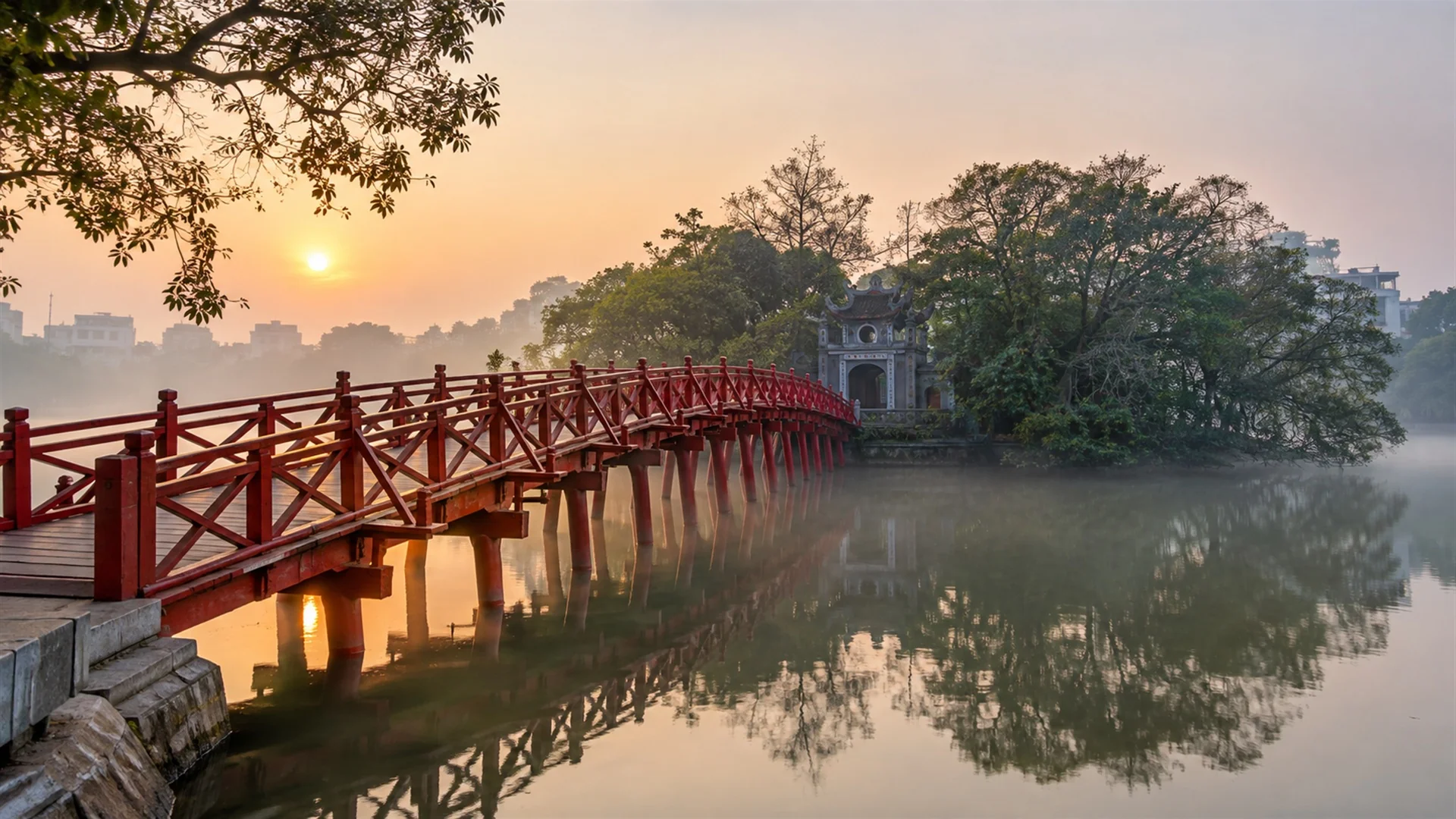 Things to do in Hanoi — red wooden bridge leading to Ngoc Son Temple on Hoan Kiem Lake at dawn, soft mist, travel photography