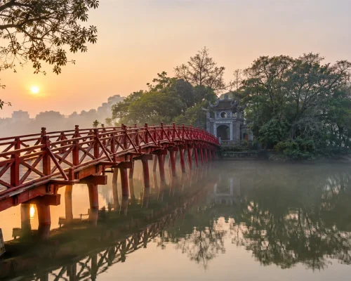Things to do in Hanoi — red wooden bridge leading to Ngoc Son Temple on Hoan Kiem Lake at dawn, soft mist, travel photography
