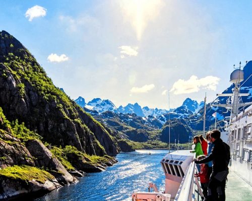 Dramatic Norwegian fjord at midnight sun with steep green mountains reflecting in still dark blue water and small expedition