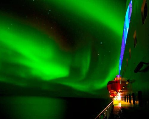 Northern lights aurora borealis green curtain dancing over Norwegian Arctic fjord with snow-covered mountains and expedition