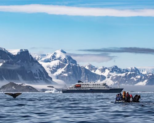 Antarctic Peninsula icebergs and glaciers with expedition ship navigating between massive blue ice formations under overcast