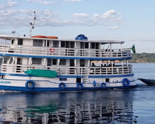 Small expedition cruise ship anchored on the Rio Negro in the Brazilian Amazon at golden hour with dense rainforest canopy re