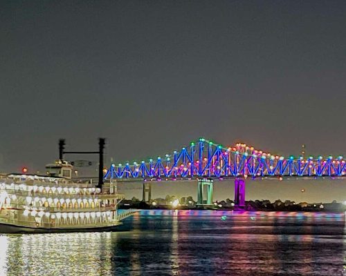 Paddlewheeler cruise ship navigating the Mississippi River at golden hour with lush green riverbanks and Spanish moss hanging