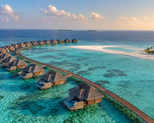 Aerial view of Maldives overwater villas stretching across turquoise lagoon with white sandbar and deep blue ocean beyond, go