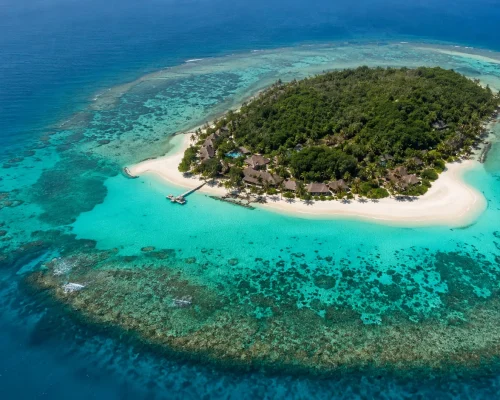 Aerial view of Fiji private island with white sand beach turquoise lagoon and lush tropical vegetation surrounded by coral re