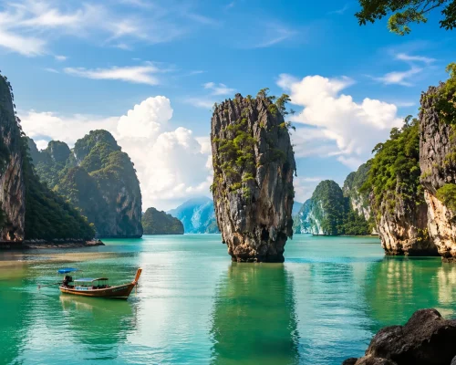 Phang Nga Bay limestone karst islands rising from emerald green Andaman water with longtail boat and tropical sky, dramatic l