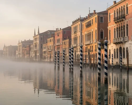 Things to do in Venice — Grand Canal at dawn with mooring poles, mist over still water and palazzo facades catching first lig